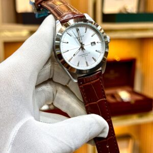 Watch with brown leather strap held by a gloved hand against a blurred background